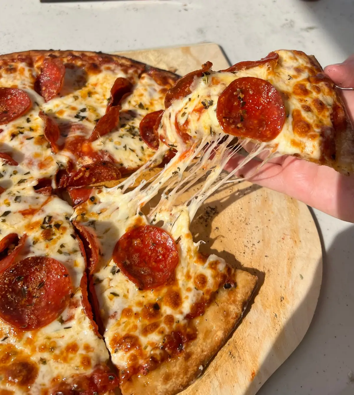 A slice of pepperoni pizza being lifted from the board in a long cheese pull