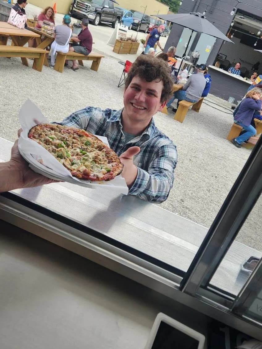 A smiling customer taking a fresh pizza through the service window of the trailer
